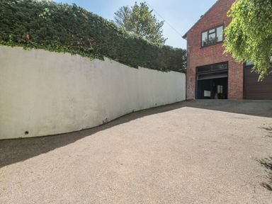 A driveway leading to a garage attached to a brick house with a white wall and tall bushes at Te Papa in North Petherton
