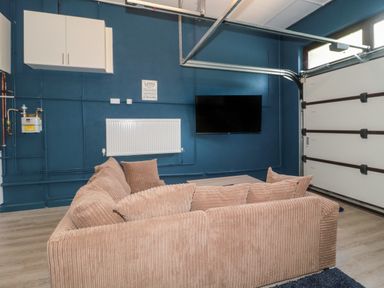A sitting area with a beige sofa a wall-mounted TV a radiator and a garage door at Te Papa in North Petherton