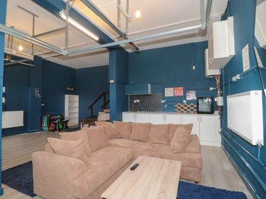 A living area with a brown sofa and wooden coffee table next to a kitchenette with white cabinets at Te Papa in North Petherton