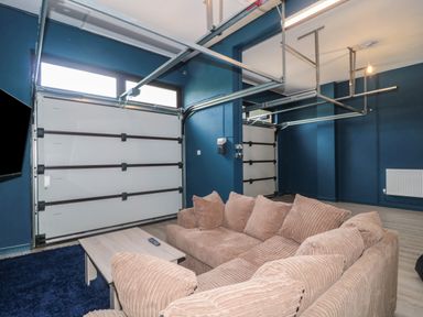 A living area with brown cushioned sofas a wooden coffee table a large blue rug garage doors and blue walls at Te Papa in North Petherton