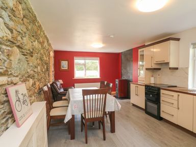 A kitchen dining area with a wooden table and chairs stone wall and modern kitchen at Curragh Cottage Rathimney near New Ross County Wexford