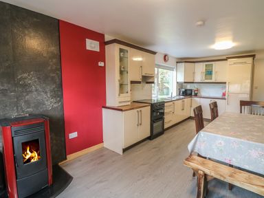 A kitchen with cream cabinets a dining table with chairs and a bench and a red stove with fire at Curragh Cottage in Rathimney near New Ross County Wexford