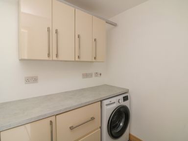 A laundry room with beige cabinets a gray countertop and a front loading washing machine at Curragh Cottage in Rathimney near New Ross County Wexford