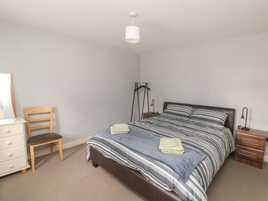 A bedroom with a double bed striped bedding two bedside tables a chair a dresser with a mirror and a clothes rack at Curragh Cottage Rathimney near New Ross County Wexford