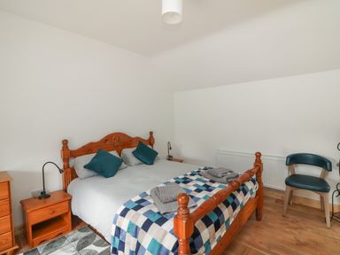 A bedroom with a wooden bed with pillows and a checkered blanket a bedside table with a lamp a chair and a radiator at Curragh Cottage in Rathimney near New Ross County Wexford