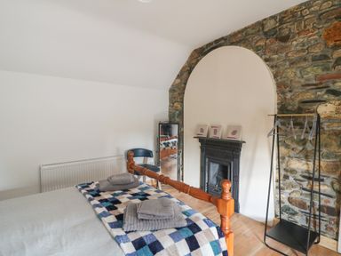 A bedroom with a wooden bed and folded towels a chair a full-length mirror a fireplace and a clothes rack at Curragh Cottage in Rathimney near New Ross County Wexford