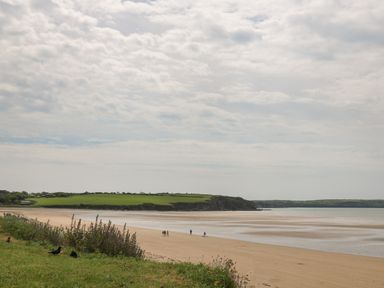 A sandy beach with people walking near the water and grassy cliffs in the background at Curragh Cottage in Rathimney near New Ross County Wexford