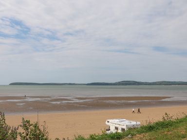 A sandy beach with people walking and a camper van parked near the shore at Curragh Cottage in Rathimney near New Ross County Wexford