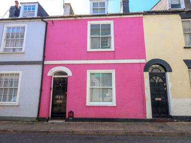 A street view of three connected houses with a pink middle house with black door and white window frames at Georgian Hideaway in Weymouth