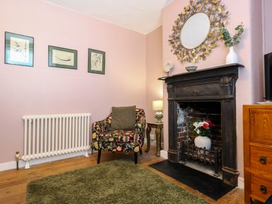 A living room with a floral armchair a fireplace with flowers and a round mirror above at Georgian Hideaway in Weymouth