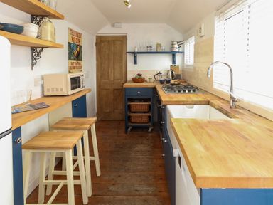 A kitchen with wooden countertops blue cabinets two stools a microwave and a wooden door at Georgian Hideaway in Weymouth