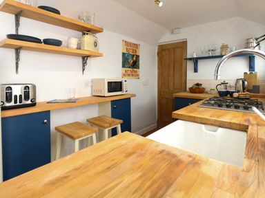 A kitchen with wooden countertops blue cabinets stools and appliances at Georgian Hideaway in Weymouth