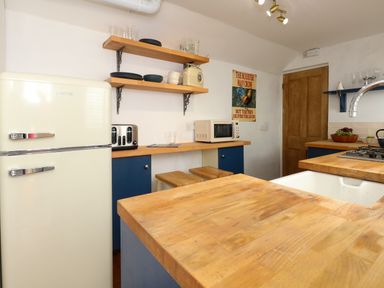 A kitchen with wooden countertops a cream fridge blue cabinets and open wooden shelves at Georgian Hideaway in Weymouth
