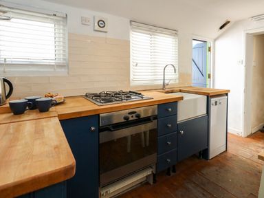 A kitchen with wooden countertops blue cabinets a gas stove oven a farmhouse sink and a dishwasher at Georgian Hideaway in Weymouth