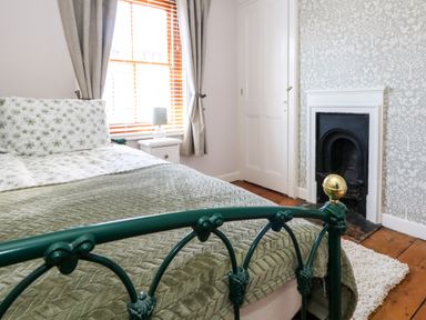 A bedroom with a green metal bed frame green blanket floral bedding a window with curtains a nightstand with a lamp and a fireplace at Georgian Hideaway in Weymouth