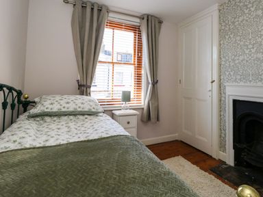 A bedroom with a single bed next to a window with curtains a nightstand lamp a fireplace and a closed door at Georgian Hideaway in Weymouth