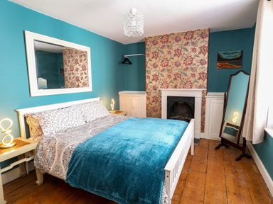 A bedroom with a double bed blue blanket bedside tables lamps a large mirror and a fireplace at Georgian Hideaway in Weymouth