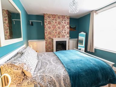 A bedroom with a bed a mirror on the wall a fireplace and a window with curtains at Georgian Hideaway in Weymouth