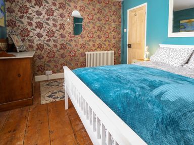 A bedroom with a white bed blue blanket floral wallpaper wooden dresser and wooden floor at Georgian Hideaway in Weymouth