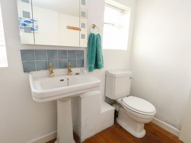 A bathroom with a white pedestal sink and a toilet with a window and a green towel at Georgian Hideaway in Weymouth