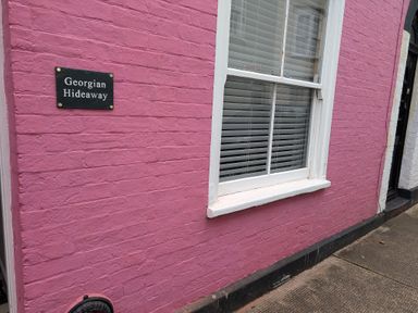 A pink brick wall with a window and a sign reading Georgian Hideaway at Georgian Hideaway in Weymouth