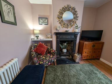 A living room with a floral armchair pillow fireplace mirror television on wooden cabinet and green rug at Georgian Hideaway Weymouth
