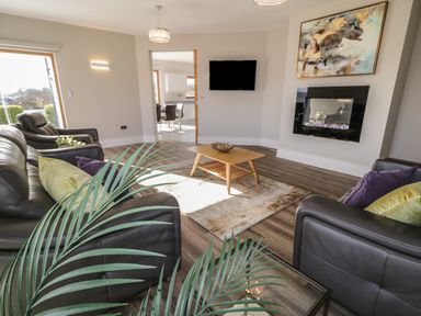 A living room with leather sofas a wooden coffee table a wall-mounted TV an electric fireplace and a large window at Moorhen House in Loughanure near Annagry County Donegal