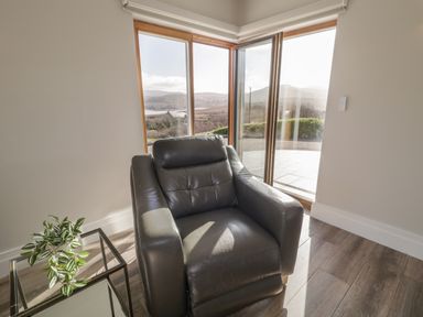A room with a black leather armchair next to a glass side table with a plant by large windows at Moorhen House in Loughanure near Annagry County Donegal