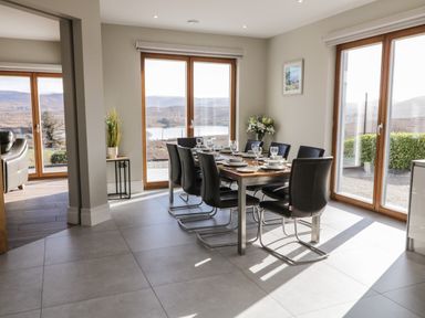 A dining area with a table set for eight and large windows overlooking hills and water at Moorhen House in Loughanure near Annagry County Donegal