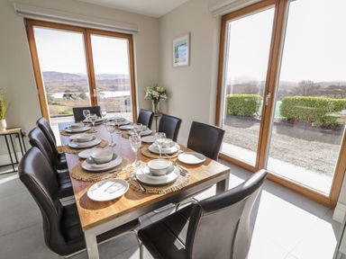 A dining room with a wooden table set for eight people and large windows showing outdoor landscape at Moorhen House Loughanure near Annagry County Donegal