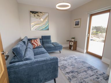 A sitting room with a blue sectional sofa a patterned rug a wooden door a small bookshelf and a large window at Moorhen House in Loughanure near Annagry County Donegal