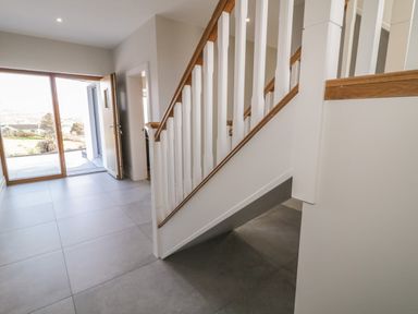 An entryway with tiled floor a staircase with white balusters and wooden handrail and an open door leading outside at Moorhen House in Loughanure near Annagry County Donegal