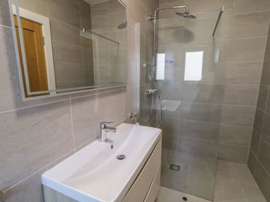 A bathroom with a white sink and faucet a large mirror and a walk in shower with glass partition