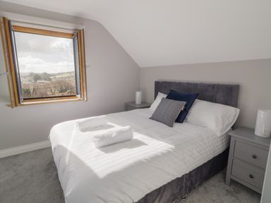 A bedroom with a double bed, two pillows, two towels on the bed, two bedside tables with lamps and an open window showing a view outside at Moorhen House in Loughanure near Annagry County Donegal