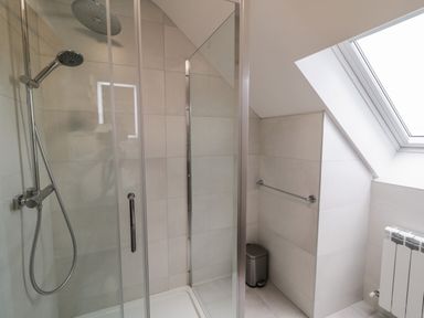 A bathroom with a glass shower enclosure a showerhead a towel rail a trash bin and a window at Moorhen House in Loughanure near Annagry County Donegal