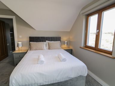 A bedroom with a bed with white linens two rolled towels bedside tables with lamps and a window at Moorhen House in Loughanure near Annagry County Donegal