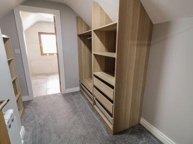 A walk-in closet with wooden shelves and drawers next to a door leading to a tiled room at Moorhen House in Loughanure near Annagry County Donegal