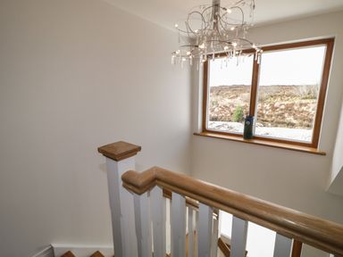 A staircase with wooden handrails and white spindles next to a window with a landscape view at Moorhen House in Loughanure near Annagry County Donegal