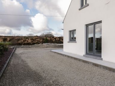 A gravel driveway beside a white house with grey windows and a stone wall in the background at Moorhen House in Loughanure near Annagry County Donegal