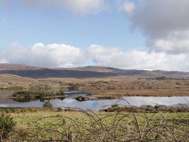 A rural landscape with a lake and small island surrounded by hills under a partly cloudy sky at Moorhen House in Loughanure near Annagry County Donegal