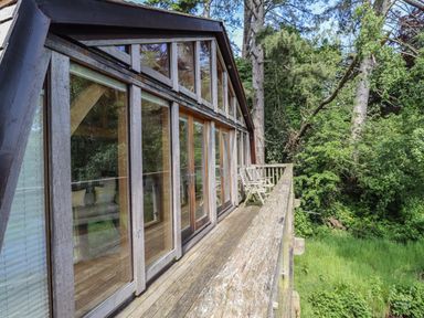 A wooden balcony with two chairs outside large glass doors surrounded by trees at The Boathouse in Belford