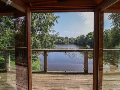 A wooden balcony overlooking a lake surrounded by trees at The Boathouse in Belford