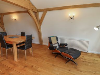 A room with a wooden dining table and black chairs and a black lounge chair with a throw on wooden floor at The Boathouse in Belford