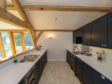 A kitchen with black cabinets white countertops wooden beams and large windows at The Boathouse in Belford