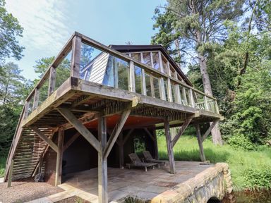 A wooden elevated house with glass railings surrounded by trees and grass at The Boathouse in Belford