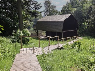 A wooden boardwalk leading to a boathouse surrounded by grass and trees at The Boathouse in Belford