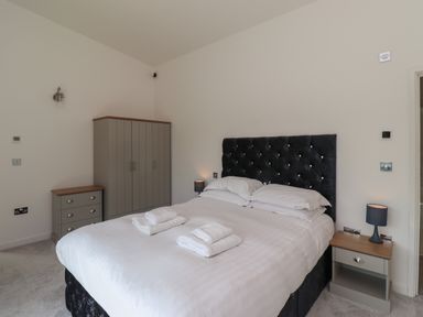 A bedroom with a bed and folded towels a nightstand with a lamp a wardrobe and a chest of drawers at Otters Cove in Belford