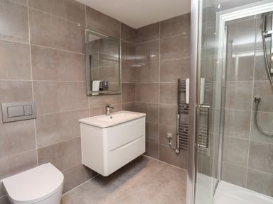 A bathroom with a toilet, floating sink with mirror, heated towel rail and glass shower enclosure at Otters Cove in Belford