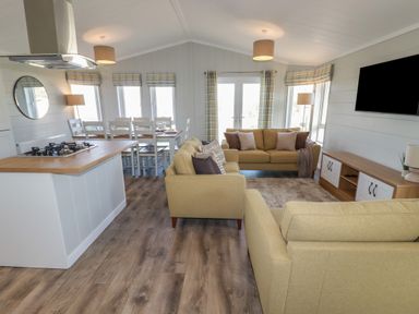 An open plan living and dining area with beige sofas a dining table and kitchen island at 4 Meadow Retreat in Dobwalls