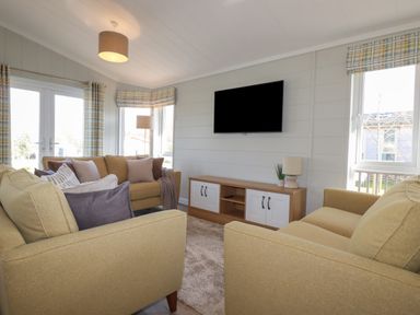 A living room with two yellow sofas, a TV mounted on the wall, and a wooden cabinet at 4 Meadow Retreat in Dobwalls